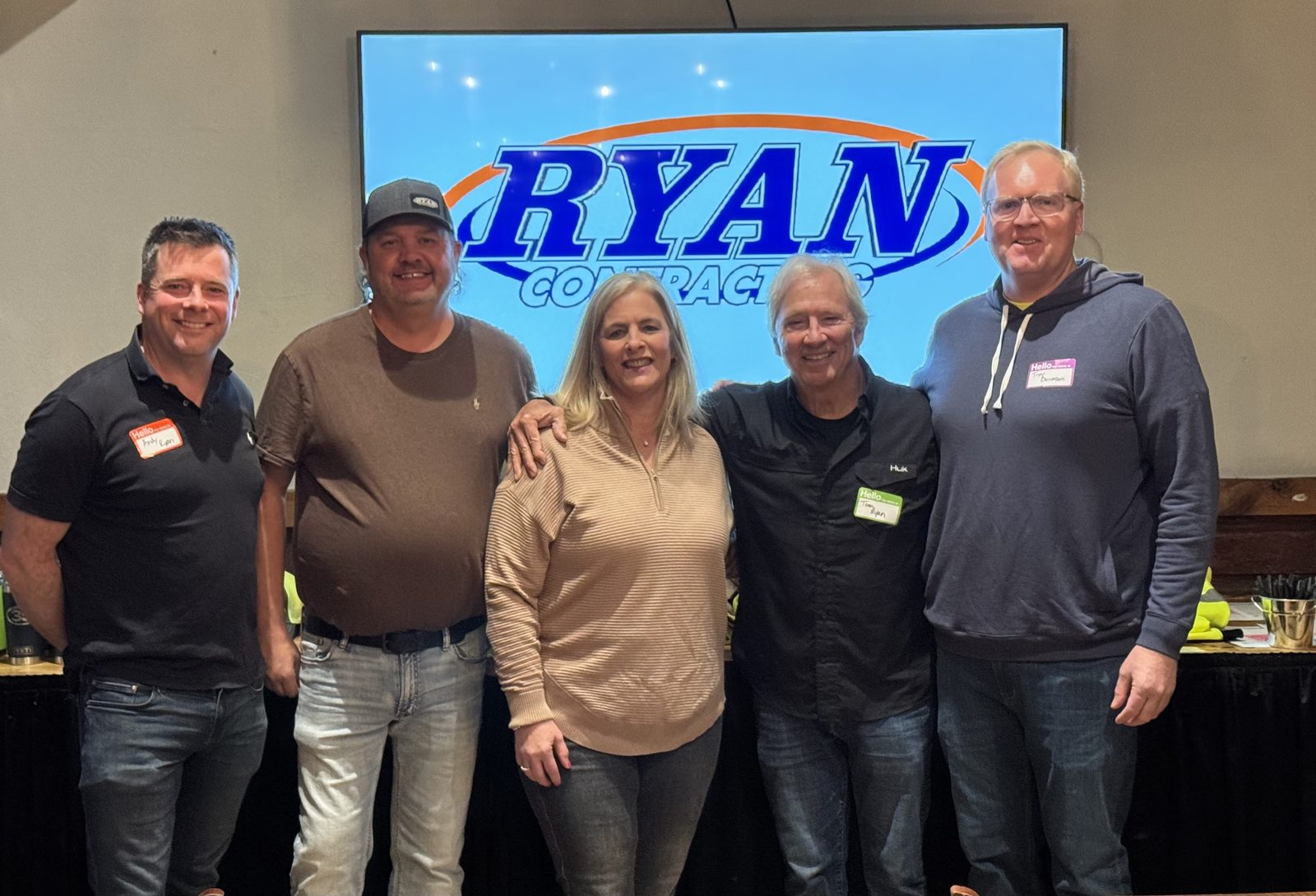 Andy Ryan, Mike, Beth, Tom Ryan and Troy Ouverson standing together in front of a Ryan Contracting logo