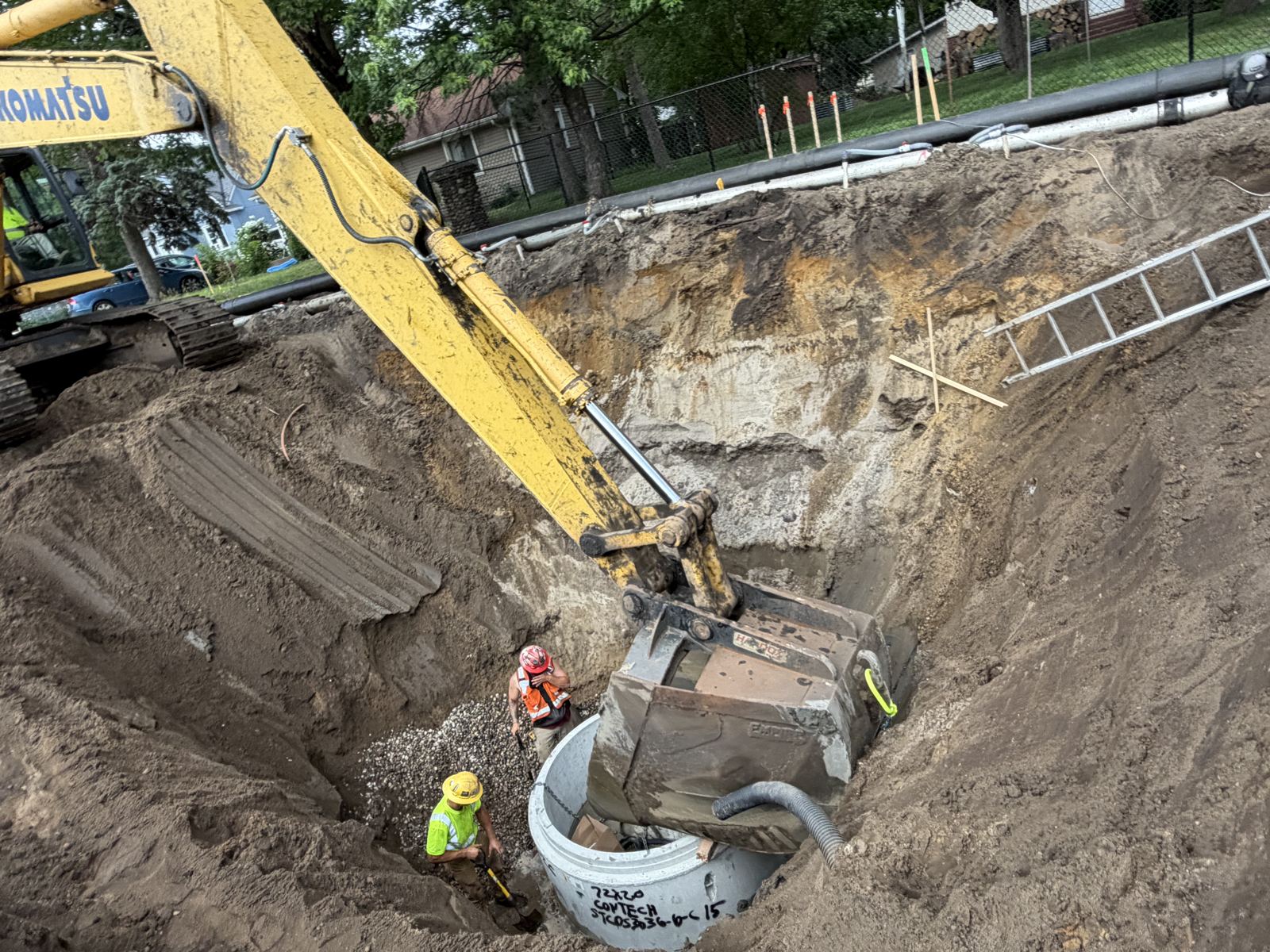 Ryan Contracting pipe crew setting a precast manhole in a deep excavation as a Komatsu excavator lowers it