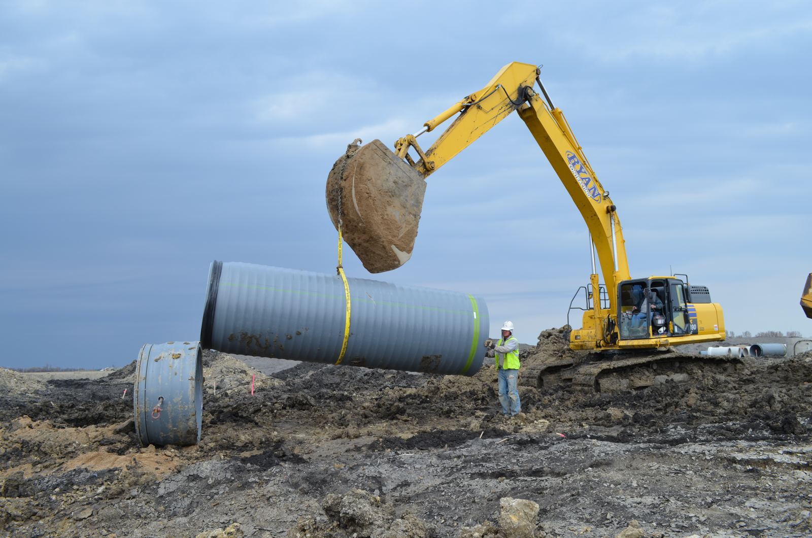 Crew guiding a large storm pipe into place as an excavator lowers it